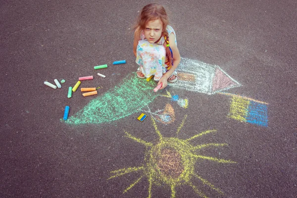 Ukrainian girl child draws children's drawings with chalk on the pavement.