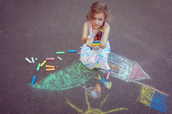 Ukrainian girl child draws children's drawings with chalk on the pavement.