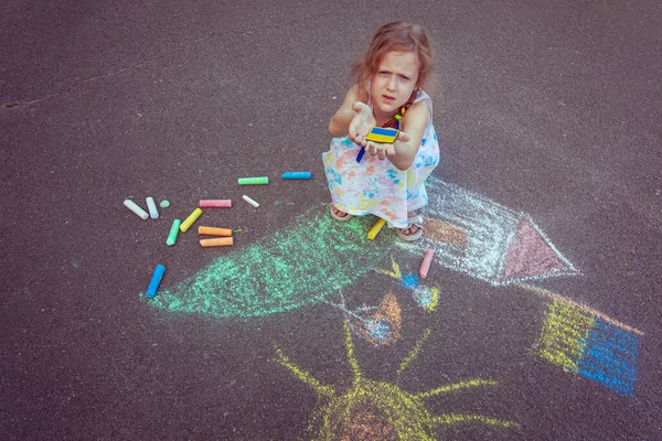 Ukrainian girl child draws children's drawings with chalk on the pavement.