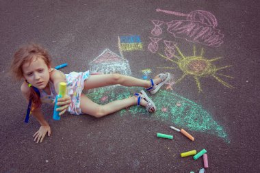 Ukrainian girl child draws children's drawings with chalk on the pavement.