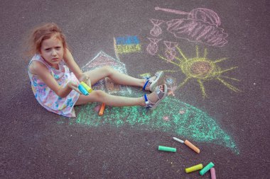 Ukrainian girl child draws children's drawings with chalk on the pavement.