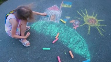 Ukrainian girl child draws children's drawings with chalk on the pavement.