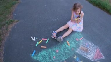 Ukrainian girl child draws children's drawings with chalk on the pavement.