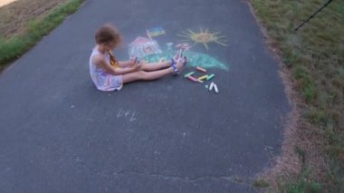 Ukrainian girl child draws children's drawings with chalk on the pavement.