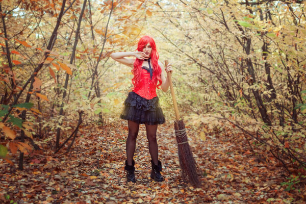 Young and beautiful witch woman with a broom in the autumn forest.