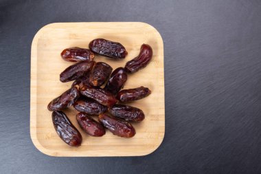 Kurumuş hurmalar siyah bir taş levha üzerinde bambu bir tabakta. sağlıklı yemek için organik meyveler