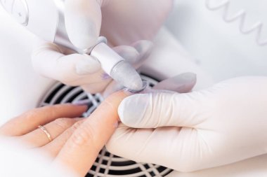 Elektrik dosyasıyla çivi işleme. Manikürcü tırnak cilasını matkapla söküyor. Profesyonel bir manikür yaratmak.