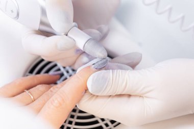 Elektrik dosyasıyla çivi işleme. Manikürcü, bir tırnak matkabıyla müşterinin tırnağındaki cilayı çıkarıyor. manikür oluşturma