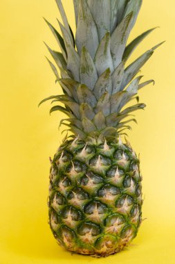 Sarı arka planda yaprakları olan işlenmemiş olgun ananas meyvesi..