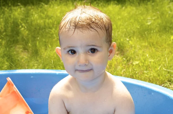 Young child having fun in a paddling pool in the garden. — Stock Photo, Image