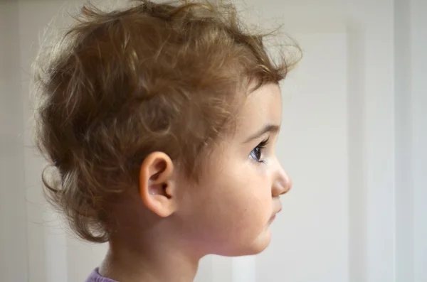 金髪の巻き毛の女の子の幼児の若い金髪子サイド プレーン背景で撮影。彼女は遠くを見ています。美しい。ヘッド ショット. — ストック写真