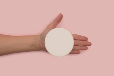 Bir kadının elinde kremalı beyaz plastik bir kavanoz vardır..