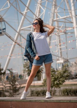 Yazın dönme dolabın yanında eğlenen kız. Şort ve tişörtle..