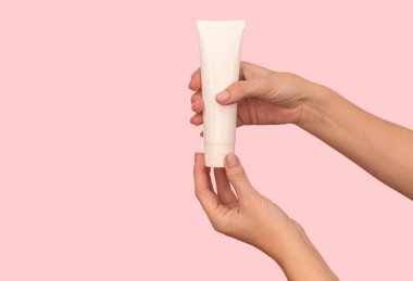 Ellerinde kozmetik kremi olan beyaz bir kap var. Vücut bakımı için. Pembe bir arka planda.