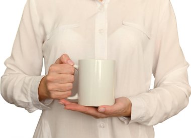 Female hands in a white shirt are holding a white mug. Mockup. Close-up.