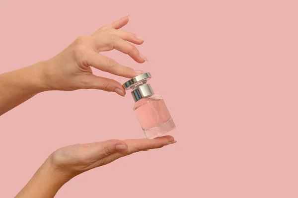 Kadın elleri cam bir kap tutuyor. Modern moda ürünü. Pembe bir arka planda.