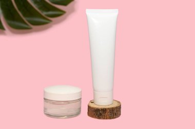 Cam ve plastik ambalajlı doğal kozmetik kremi. Cilt kremi. Pembe arka planda, yeşil bir yaprak..