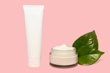 Kozmetik beyaz krem ve yeşil yapraklar pembe arka planda.