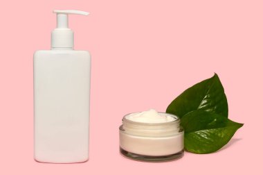 Kozmetik beyaz krem ve yeşil yapraklar pembe arka planda.