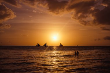 Sailingboats and silhouette of couple against a beautiful sunset clipart