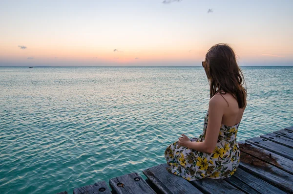 Jovem mulher sentada no cais à beira-mar no belo pôr do sol — Fotografia de Stock