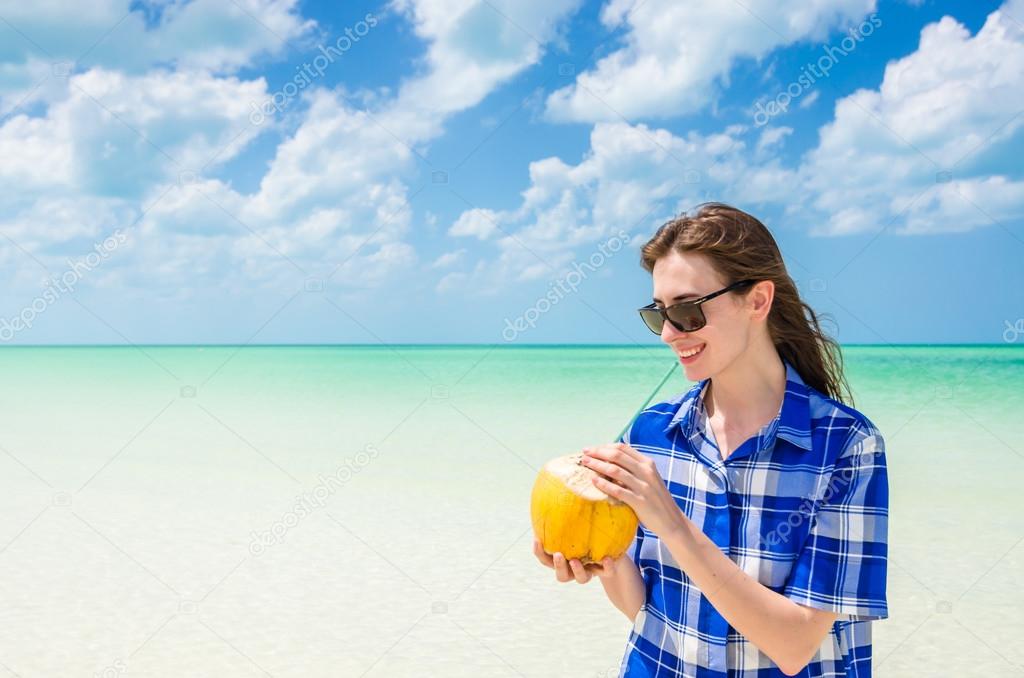 Young woman drinking coconut water against the background of turquoise sea at tropical beach during Caribbean vacation