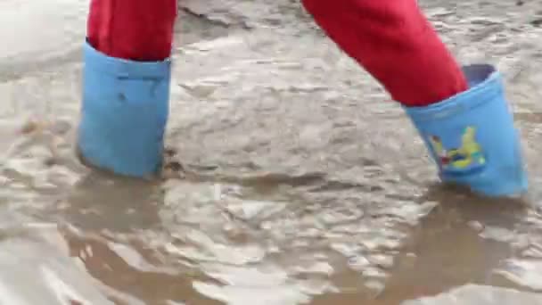 Kind voeten in rubber laarzen lopen plas vuil — Stockvideo