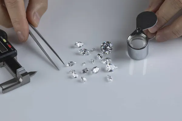 Close up of diamond experts hand at workplace evaluating gemstones polished diamonds.