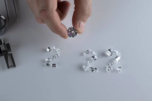 Process of laying out the number 2022 from diamonds of different sizes and shapes using tools at workplace of diamond dealer. Concept of diamond business 2022. — Fotografia de Stock