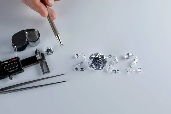 Process of laying out the number 2022 from diamonds of different sizes and shapes using tools at workplace of diamond dealer. Concept of diamond business 2022. — стоковое фото