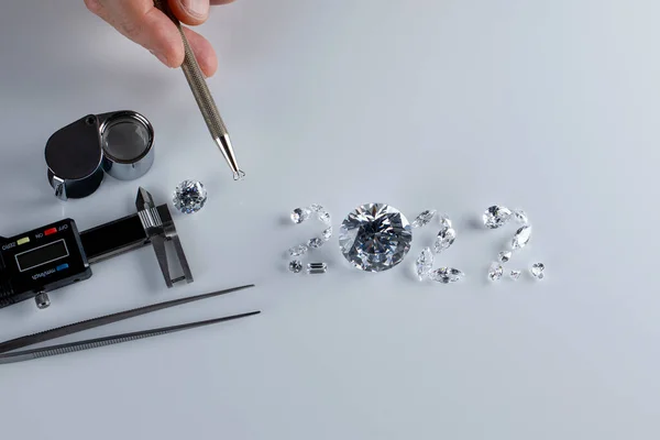 Process of laying out the number 2022 from diamonds of different sizes and shapes using tools at workplace of diamond dealer. Concept of diamond business 2022.