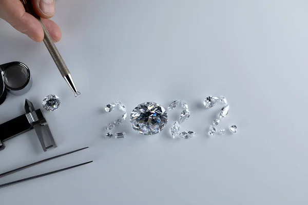 Process of laying out the number 2022 from diamonds of different sizes and shapes using tools at workplace of diamond dealer. Concept of diamond business 2022. — Foto Stock