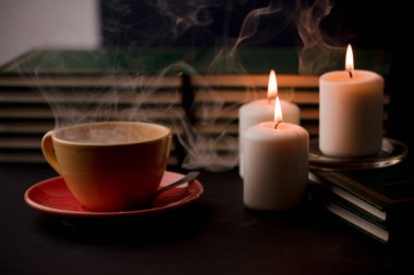 Sıcak dumanlı bir fincan kahve ve üç yanan mum. evdeki masada, elektrik kesintisi (fincana odaklan).