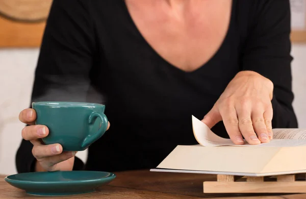 Groene Beker Met Warme Koffie Handen Van Vrouw Met Leesboek — Stockfoto