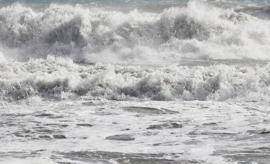 Büyük dalgalar kıyıya vuruyor, beyaz köpükle