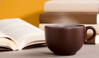 Sıcak buharlı çay ya da kahve masası, açık kitaplar, turuncu sarı arka plan.