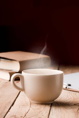 beyaz fincanda çikolata, çay ya da kahve, sıcak buhar, kırmızı arka planda kırsal ahşap masa kitapları.