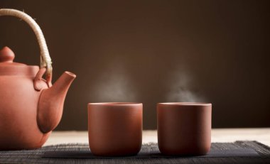 İki fincan sıcak kahverengi kireç çayı, ahşap masa üzerinde kısmi çaydanlık manzaralı. kahverengi arka plan. Metin için boşluk.