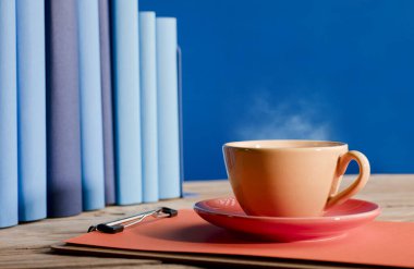 Sarı kahve ya da sıcak buharlı çay, not defterinde, açık mavi kitaplarla ve mavi arka planla..