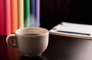 Sıcak buharlı bir fincan kahve ya da çay masanın üstünde lgtbi bayrağı renginde kitaplar..
