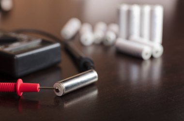 Volt hesap makineli pil, voltmetre, kırmızı pozitif direk, siyah negatif direk, ahşap çalışma masasında.