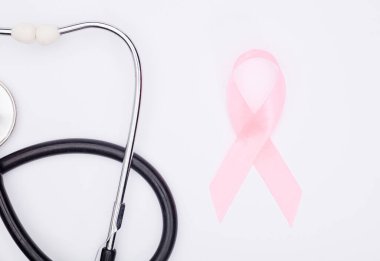Pembe kanser kurdelesi, steteskop, beyaz arka plan, göğüs kanseri farkındalığının uluslararası sembolü ve kadınlar için moral desteği. İzole edilmiş arkaplan,