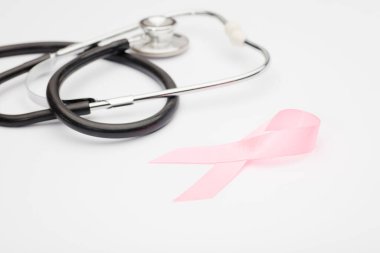 Pembe kanser kurdelesi, steteskop, beyaz arka plan, göğüs kanseri farkındalığının uluslararası sembolü ve kadınlar için moral desteği. İzole edilmiş arkaplan,