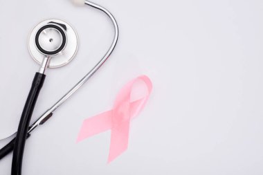 Pembe kanser kurdelesi, steteskop, beyaz arka plan, göğüs kanseri farkındalığının uluslararası sembolü ve kadınlar için moral desteği. İzole edilmiş arkaplan,