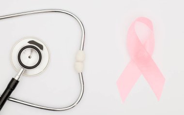 Pembe kanser kurdelesi, steteskop, beyaz arka plan, göğüs kanseri farkındalığının uluslararası sembolü ve kadınlar için moral desteği. İzole edilmiş arkaplan,