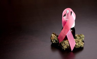 Pembe kurdele kanseri bir şişe yağla, marihuana tomurcuklarıyla, kahverengi ahşap masada, metin için yer açarak savaşıyor.