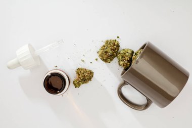 Marihuana tomurcukları fincanda, tıbbi damlalar, beyaz arka planda.
