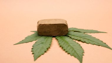portion hashish tablet with marijuana leaf, bronw background clipart