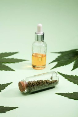 Cam kavanozda marihuana ısırığı. Damlalar içinde marihuana yağı şişesi ve yeşil yapraklar, yeşil arka plan