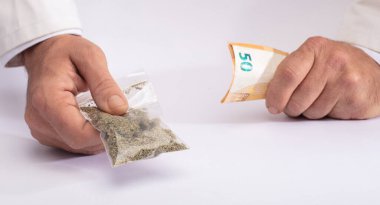 Eczacı bir çanta dolusu tıbbi marihuana verdi ve parayı diğer eliyle beyaz bir tezgahın üzerinde aldı.